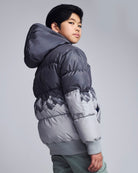 Child wearing a gray puffer jacket on a plain background