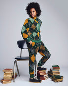 Person wearing a green and orange argyle patterned outfit sitting on a stack of books.