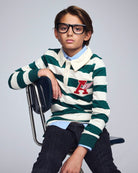 Child wearing a green and white striped sweater with a logo, sitting on a chair against a plain background