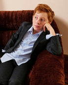 A boy wearing a navy blazer and oxford shirt, seated on a velvet chair, alternate view. Appaman Fall/Winter 2026 collection.