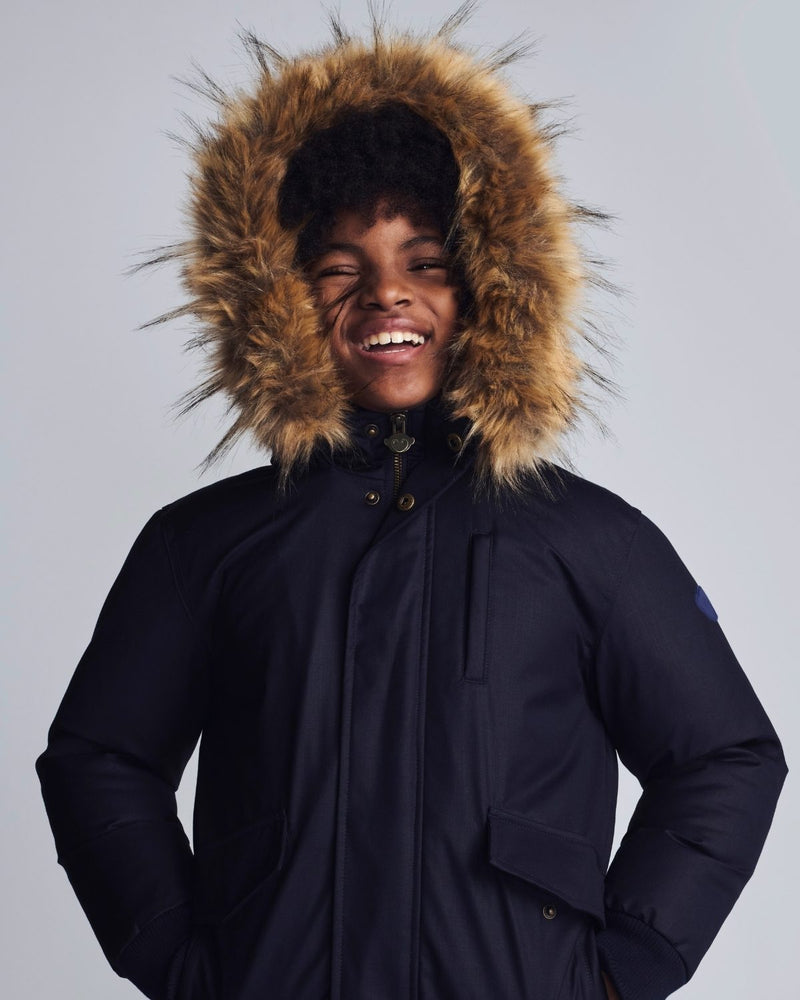 Person wearing a dark blue winter coat with a fur-lined hood on a light gray background