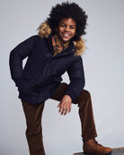 Child wearing a dark blue coat with fur hood, plaid shirt, and brown pants on a gray background