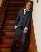 A boy wearing a navy suit, standing on a staircase. Appaman Fall/Winter 2026 collection.