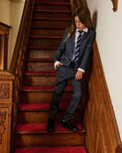 A boy wearing a navy suit, standing on a staircase. Appaman Fall/Winter 2026 collection.