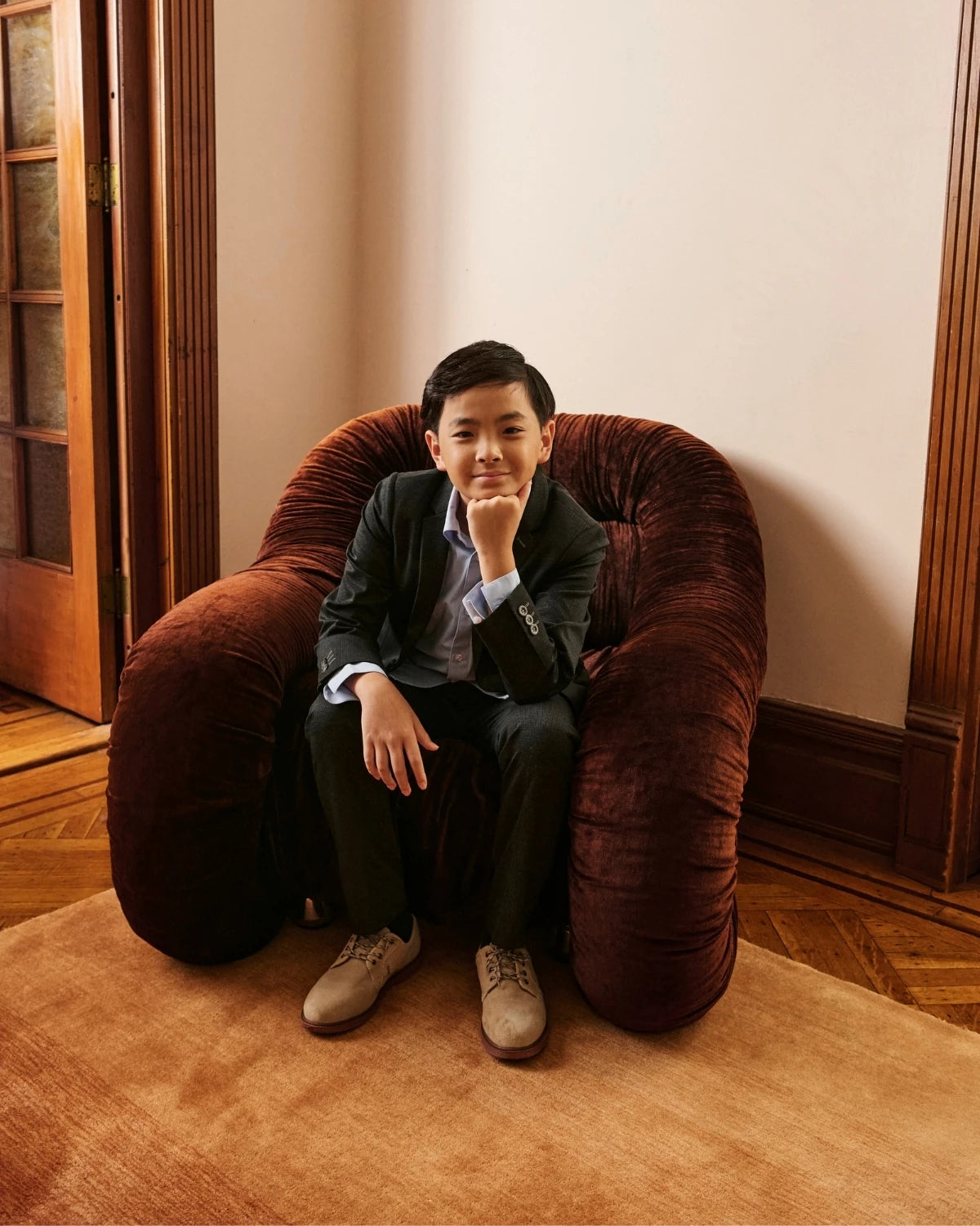 A boy wearing a navy suit, seated in a velvet chair. Appaman Fall/Winter 2026 collection.
