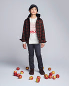 Child wearing a plaid shirt and jeans standing among apples on a gray background