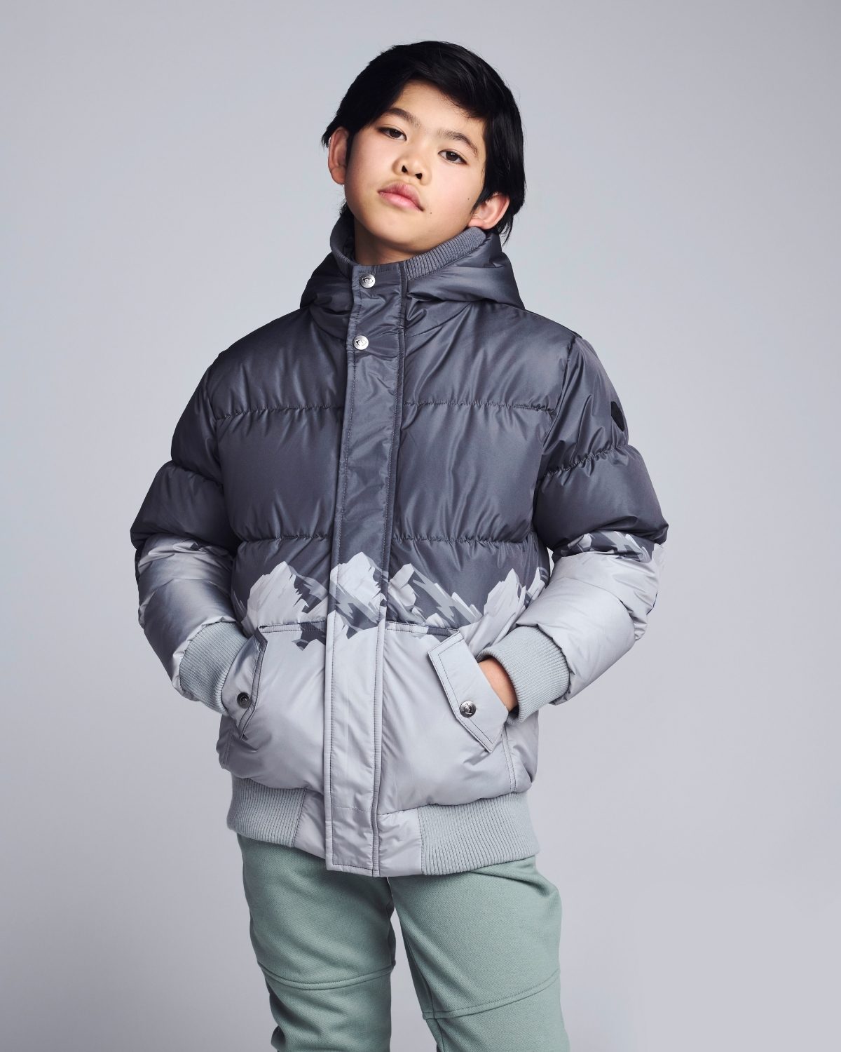 Child wearing a gray puffer jacket with mountain design on a light gray background