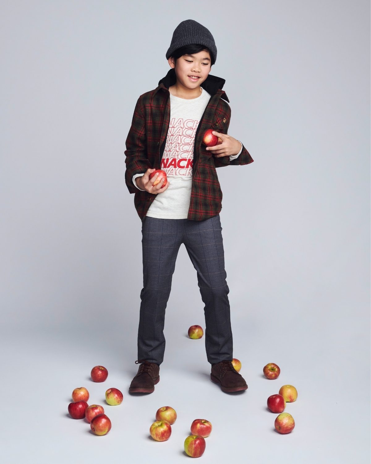 Child holding apples with a scattered pile on a plain background