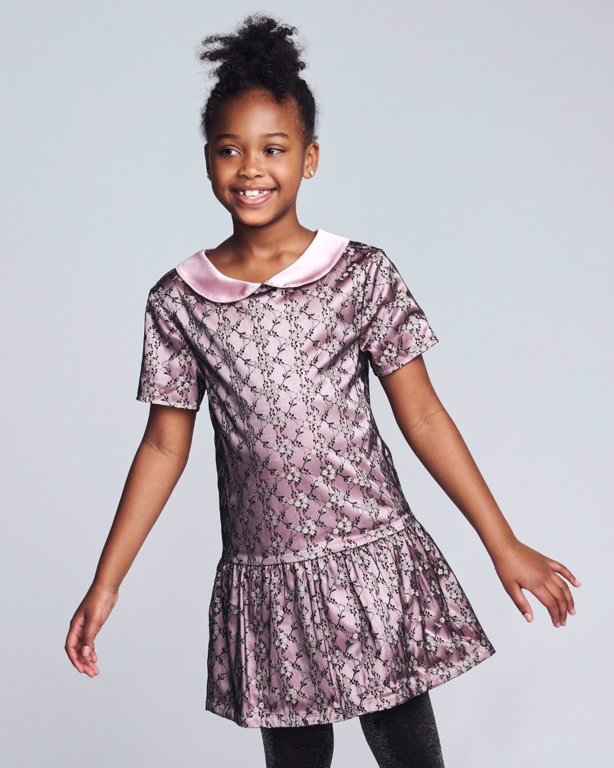Young girl wearing a floral dress with a pink collar against a light gray background