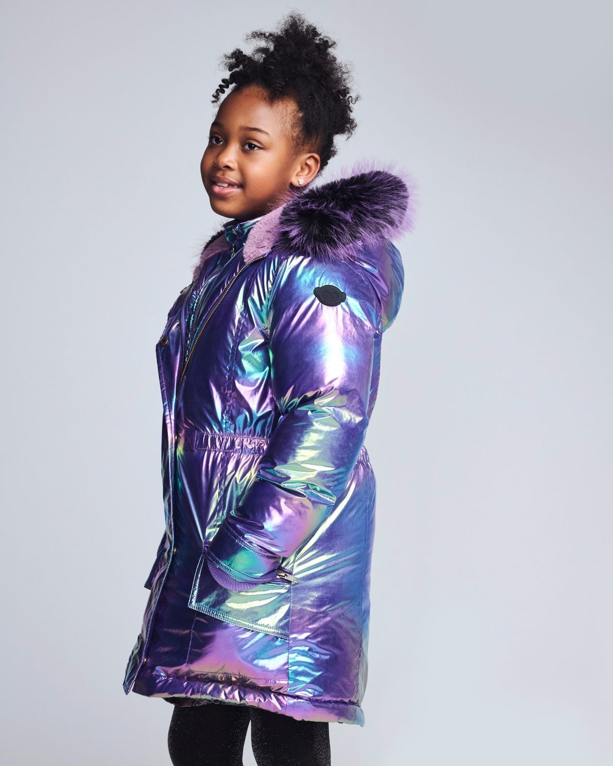 Child wearing a colorful, iridescent parka with a fur-lined hood on a plain background