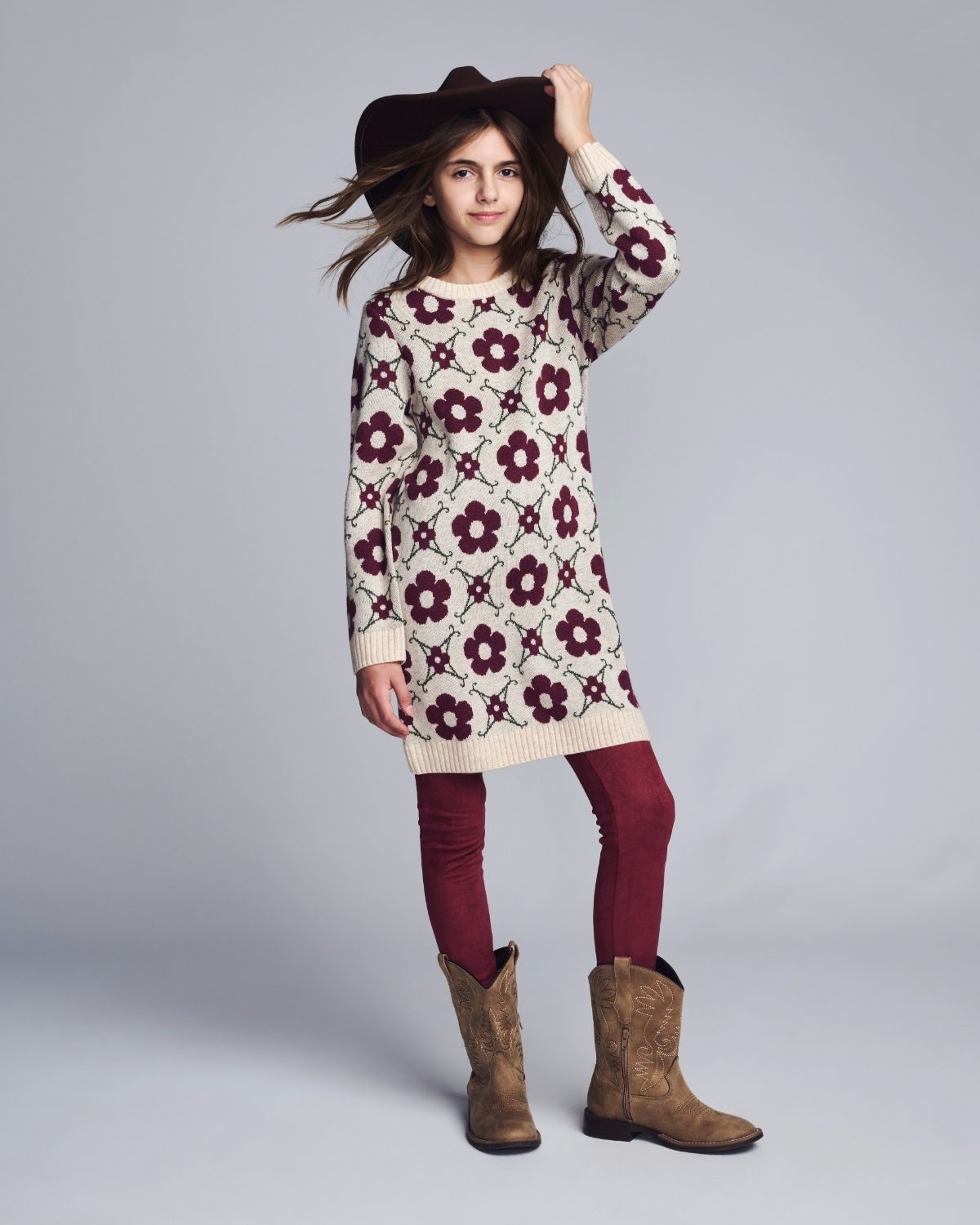 Girl wearing a floral sweater dress, burgundy leggings, and brown boots on a gray background
