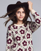 Young girl wearing a floral sweater and brown hat against a gray background