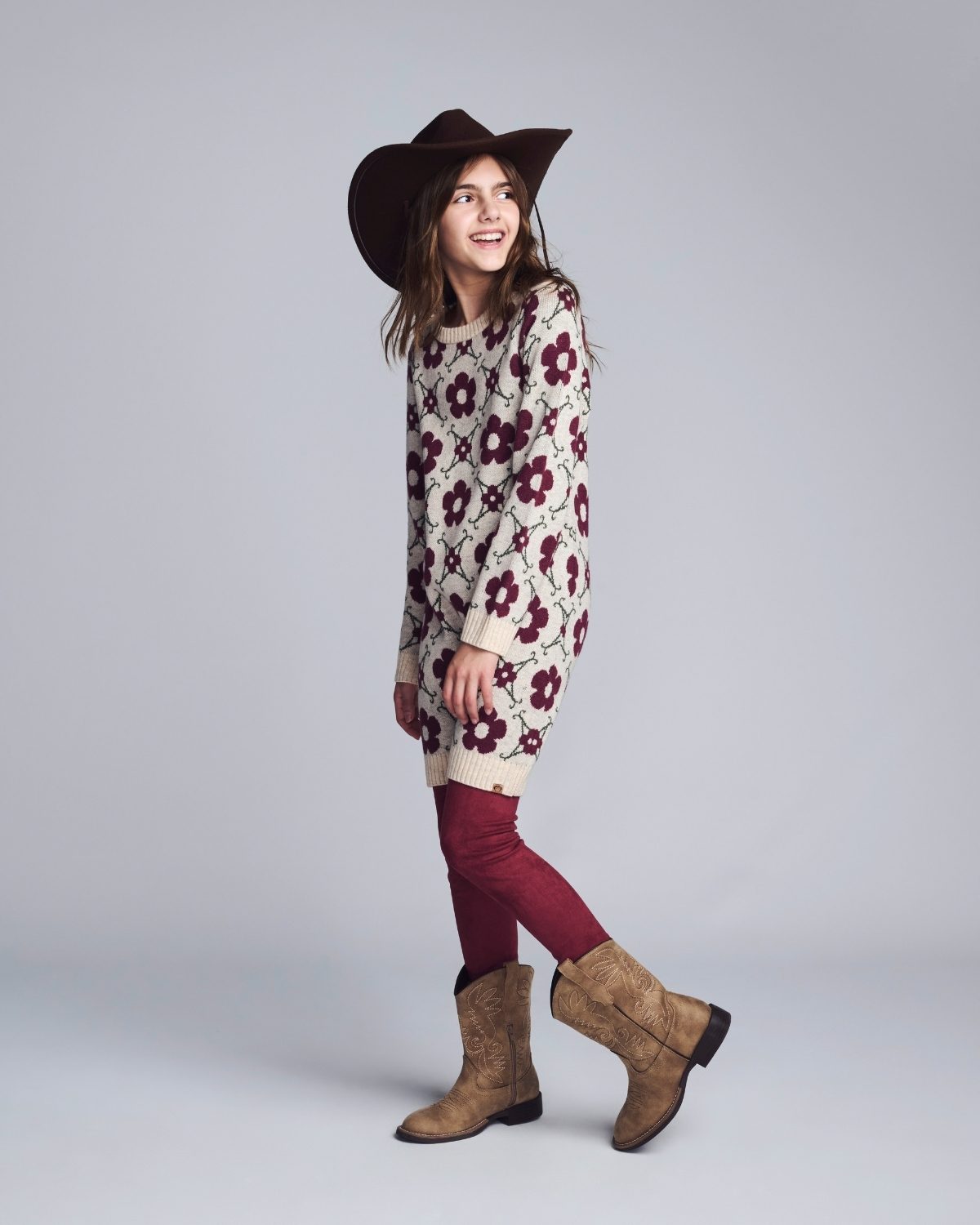 Woman wearing a floral sweater, red pants, and brown boots on a plain background