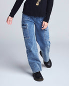 Person wearing blue jeans and black shoes on a light gray background