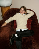 A girl wearing a cream sweater, seated on a velvet chair, alternate view. Appaman Fall/Winter 2026 collection.