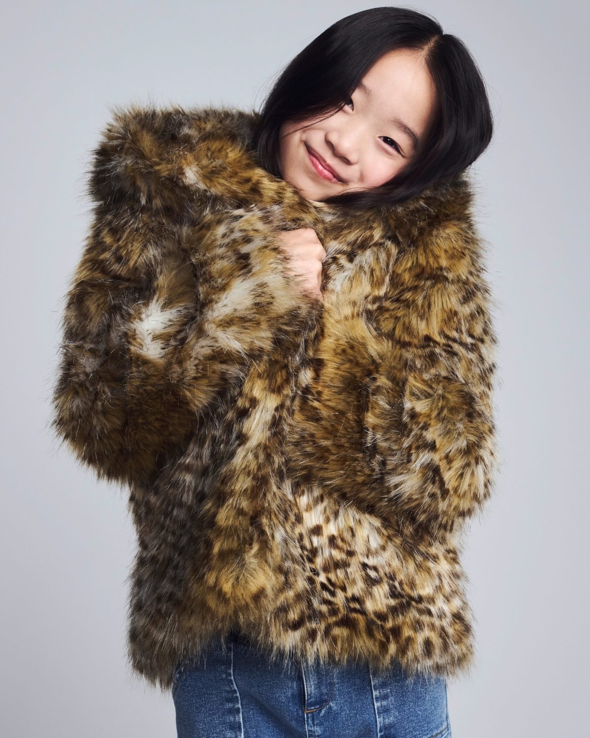 Girl wearing a leopard print fur coat against a plain background