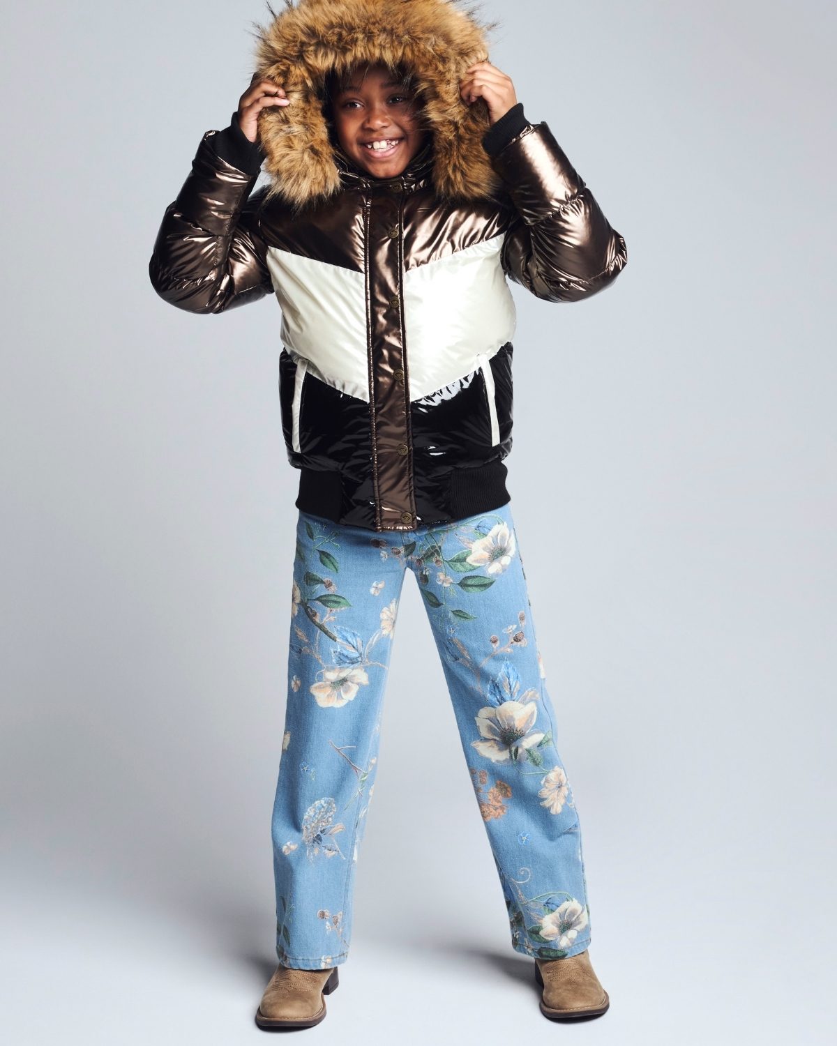Child wearing a reflective jacket with a fur-lined hood and floral pants on a light gray background