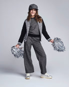 Person in gray and black varsity outfit with pom-poms on a light gray background
