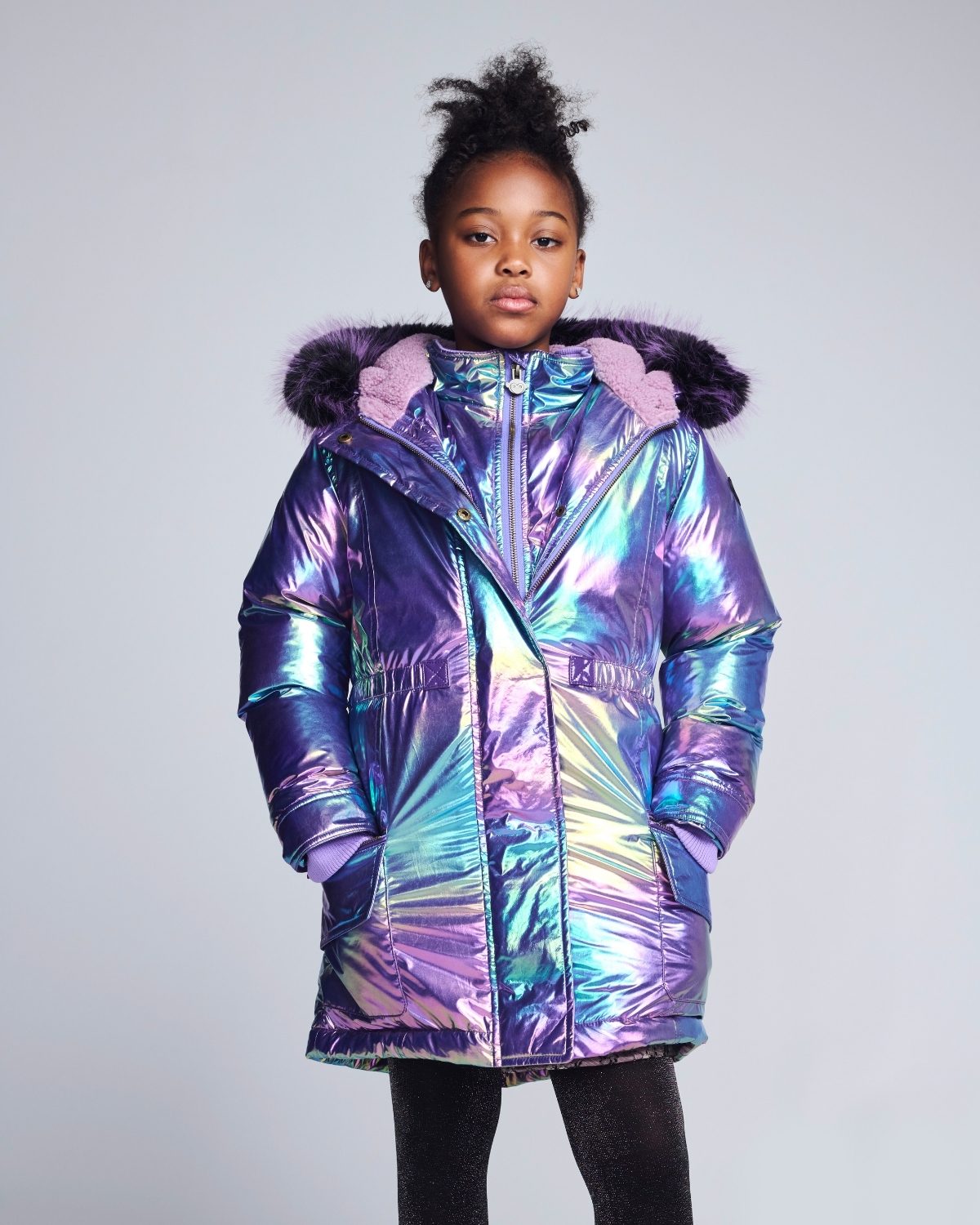 Child wearing a colorful, iridescent puffer jacket with pink fur trim on a gray background