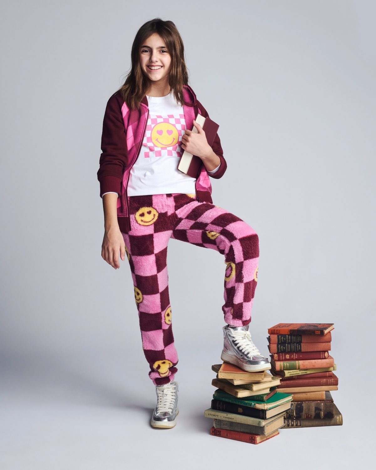 Person wearing a checkered outfit with smiley face patterns, standing on a stack of books against a plain background.
