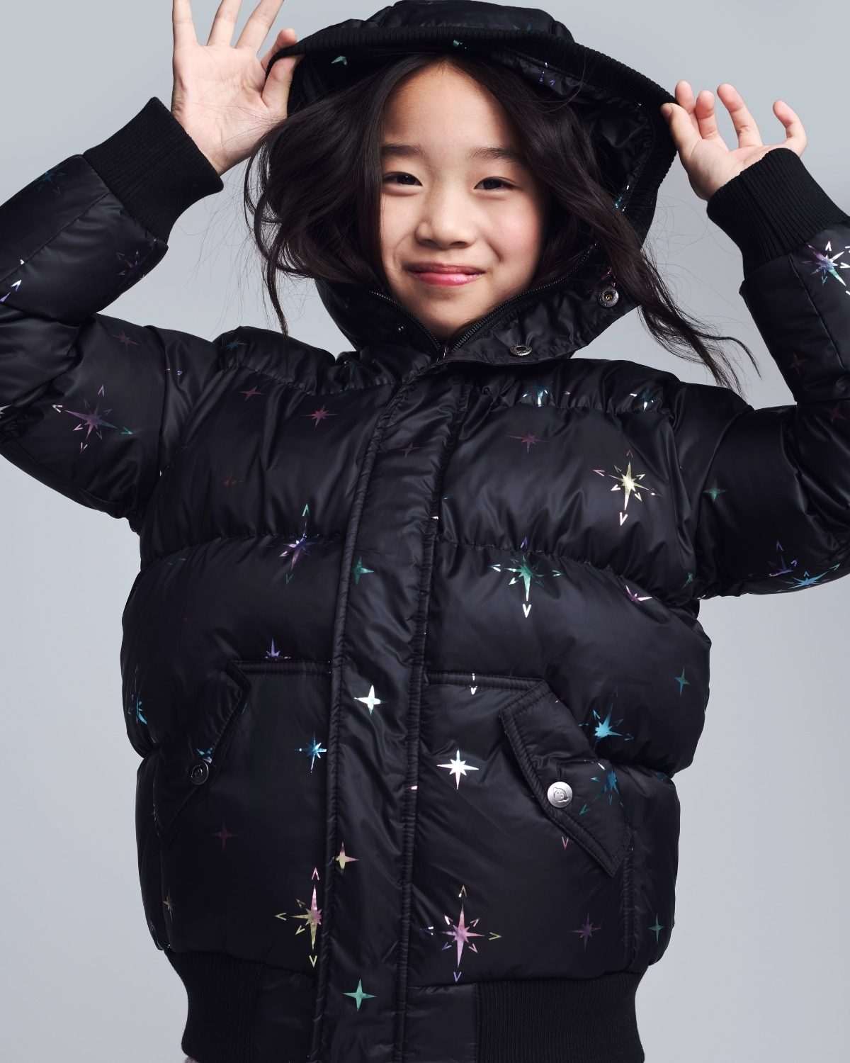 Child wearing a black puffer jacket with star patterns on a gray background