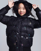 Child wearing a black puffer jacket with star patterns on a gray background