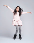 Young girl in a pink dress with arms outstretched on a plain background