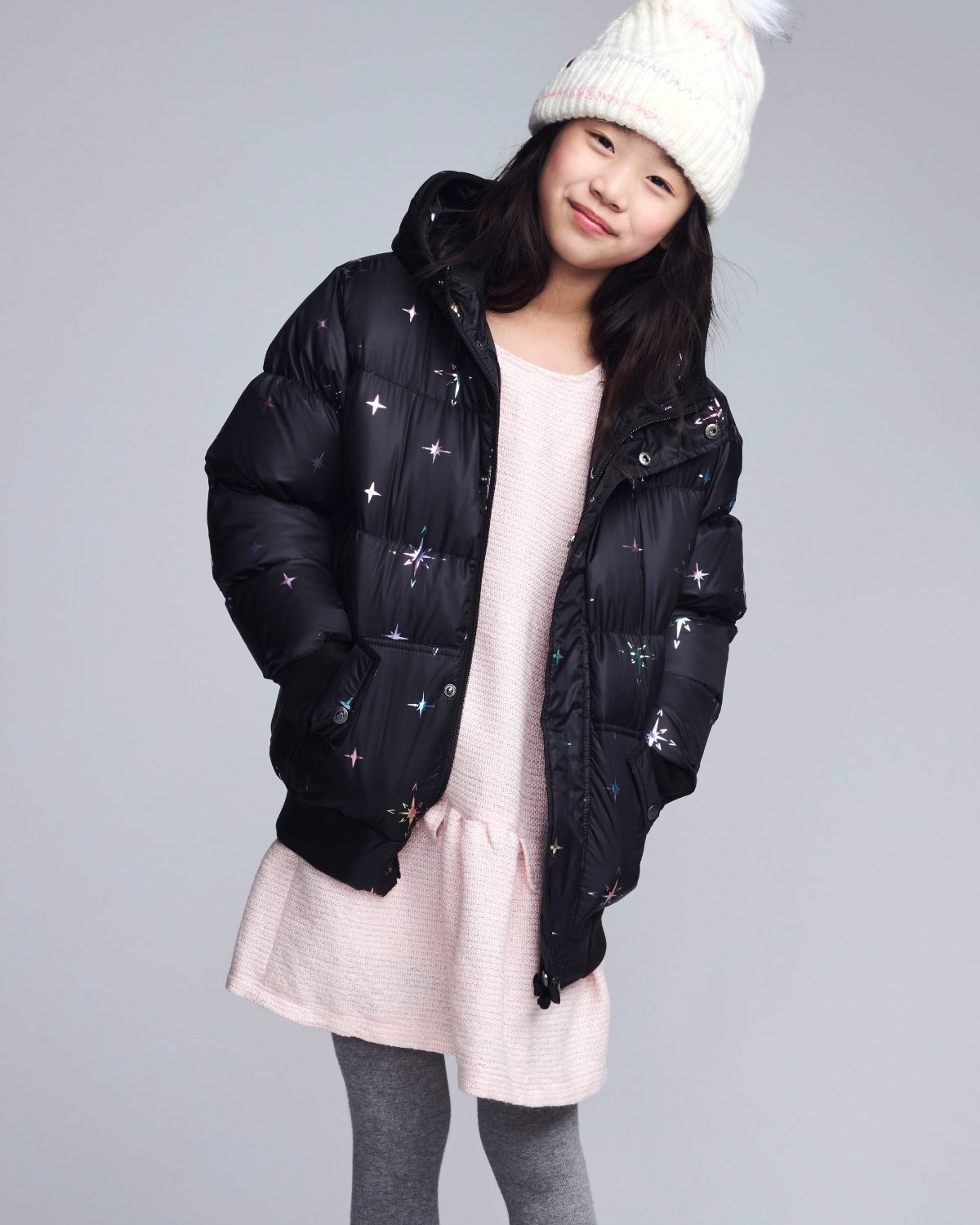 Person wearing a black puffer jacket with star patterns on a plain background