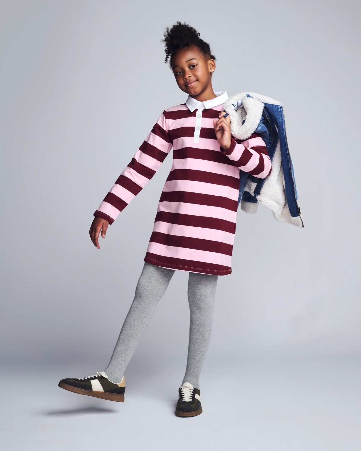 Child wearing a striped dress with gray leggings and black shoes on a plain background