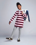 Child wearing a striped dress with gray leggings and black shoes on a plain background