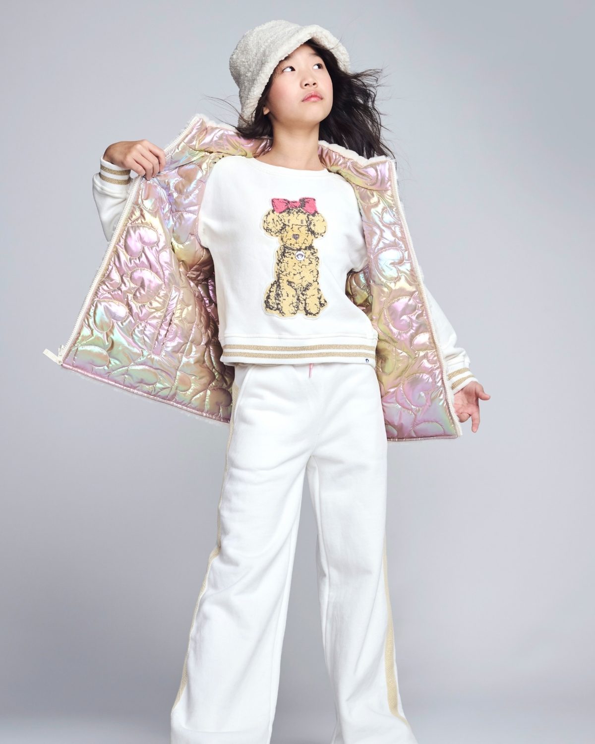 Person wearing a white outfit with a teddy bear design, holding a colorful bag on a gray background