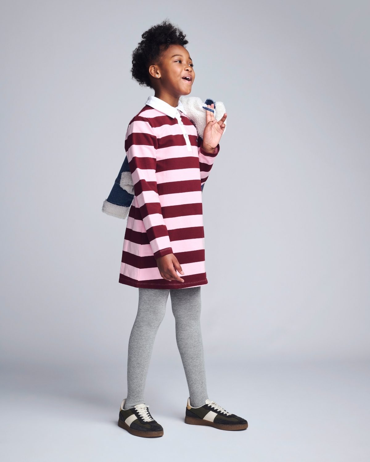 Child wearing a red and white striped dress with gray leggings on a plain background