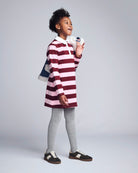 Child wearing a red and white striped dress with gray leggings on a plain background