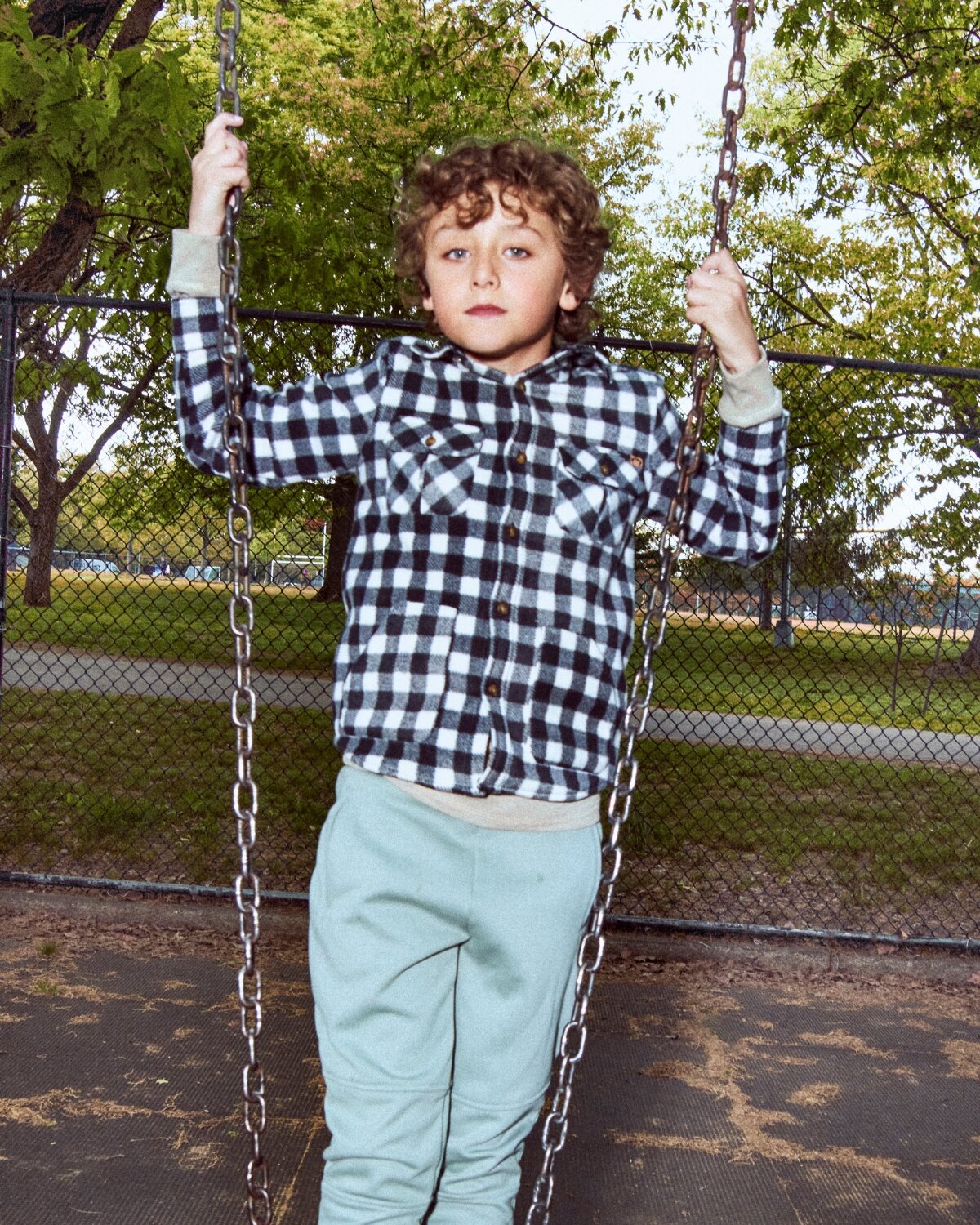 Child on a swing set in a park with trees and a fence in the background