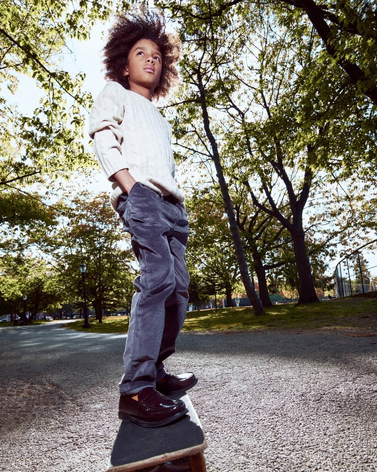Child standing on a skateboard in a park with trees and grass in the background