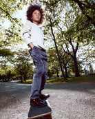 Child standing on a skateboard in a park with trees and grass in the background