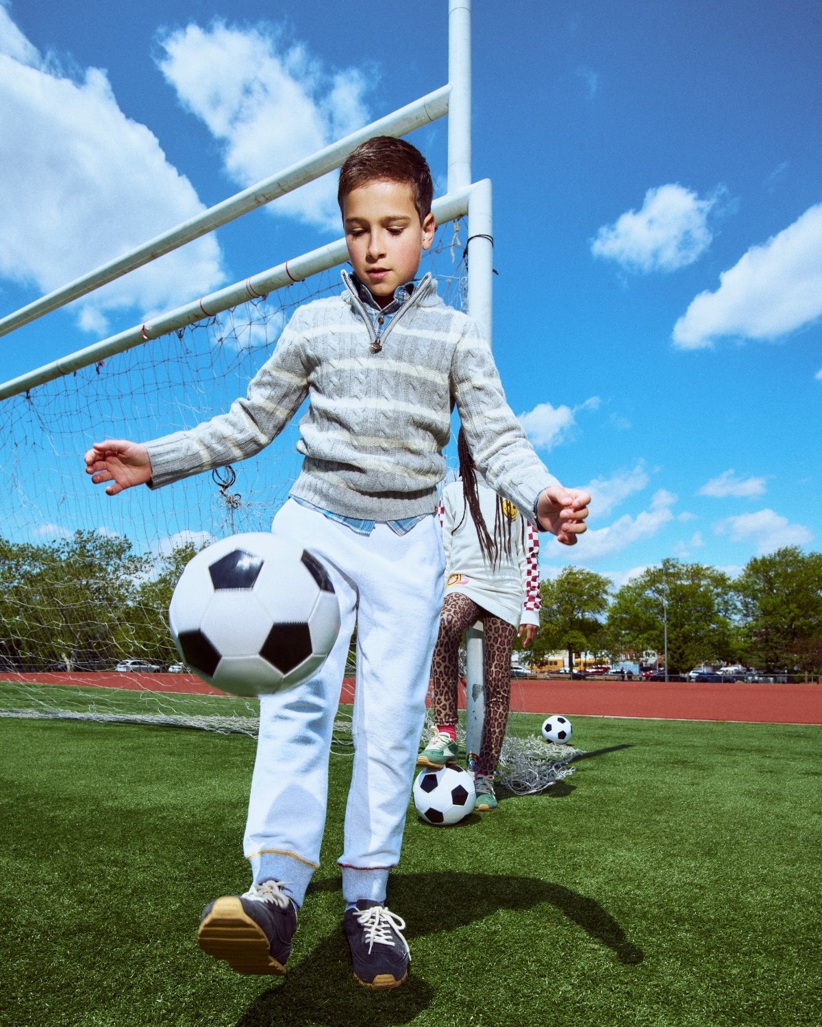 Child playing soccer on a sports field with a clear sky.