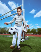 Child playing soccer on a sports field with a clear sky.