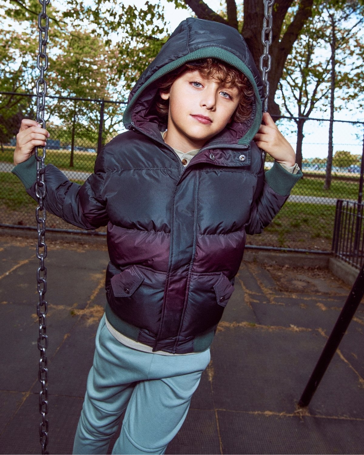Child wearing a dark jacket with a hood on a playground swing