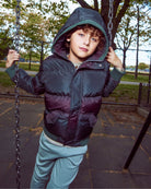 Child wearing a dark jacket with a hood on a playground swing