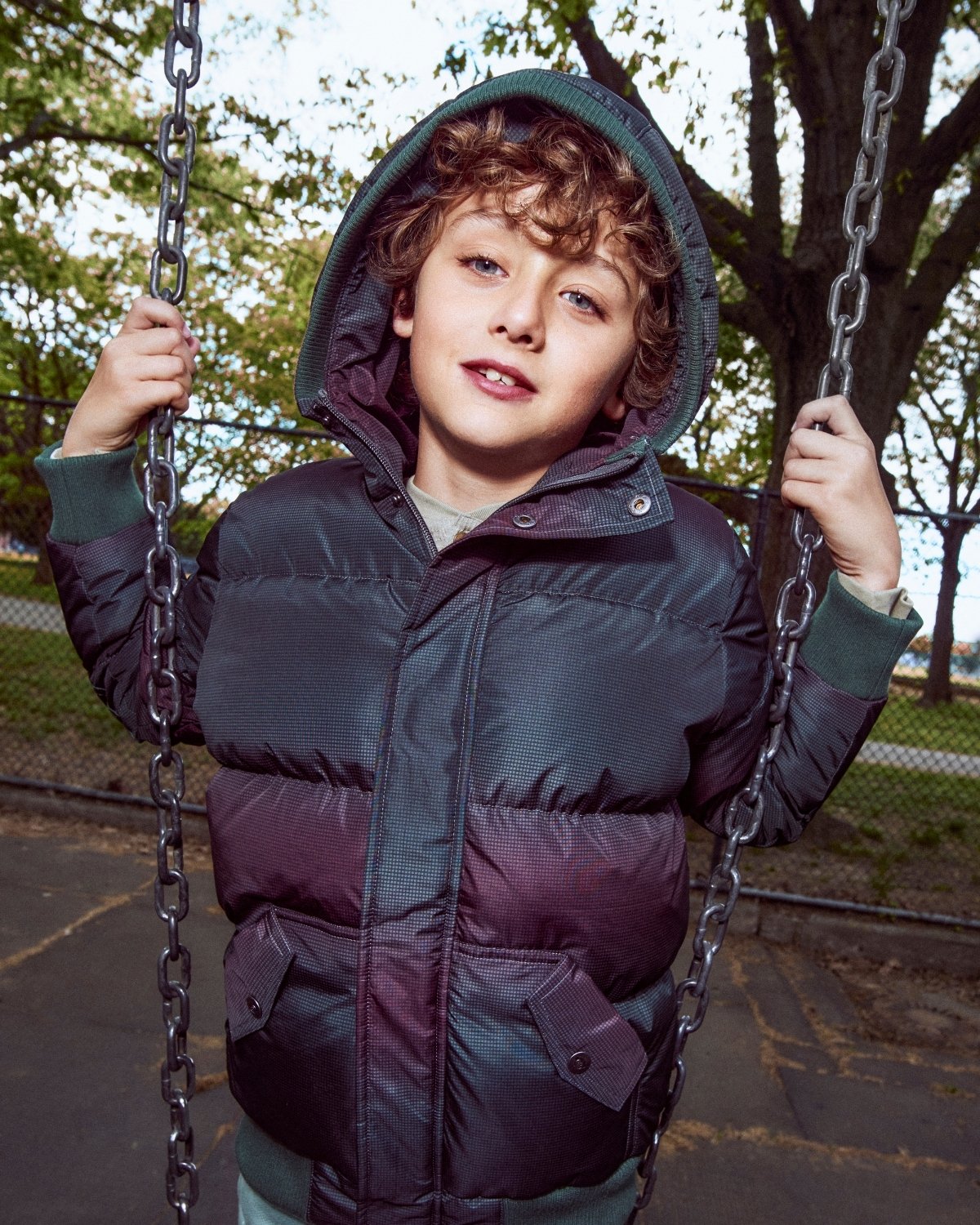 Child in a dark blue puffer jacket on a swing set with trees in the background