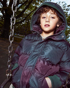 Child in a large coat on a swing set with trees in the background