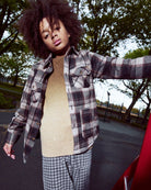 Person wearing a plaid shirt over a beige sweater with checkered pants outdoors.