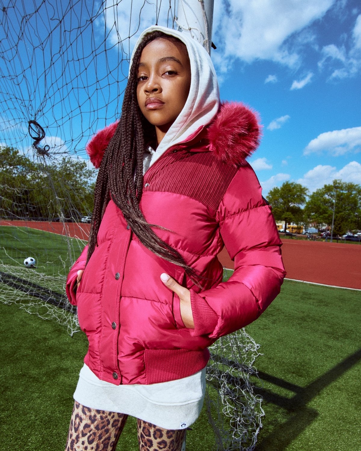 Person wearing a pink puffer jacket with a hood on a sports field.