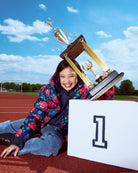 Child with trophies on a track and field, smiling at the camera