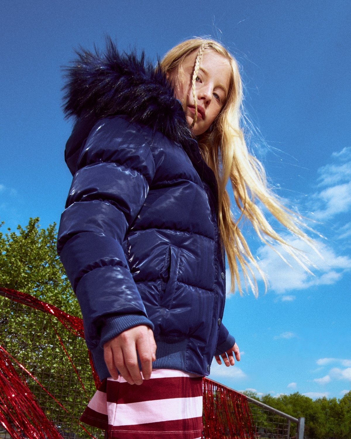 Person wearing a blue puffer jacket with a hood against a blue sky.