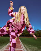 Person wearing a pink and maroon checkered outfit with smiley face patterns on a sports field.