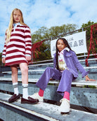 Two children in stylish outfits sitting on metal bleachers with a clear blue sky.