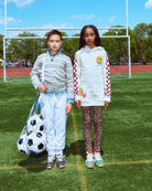 Two children standing on a soccer field with sports equipment