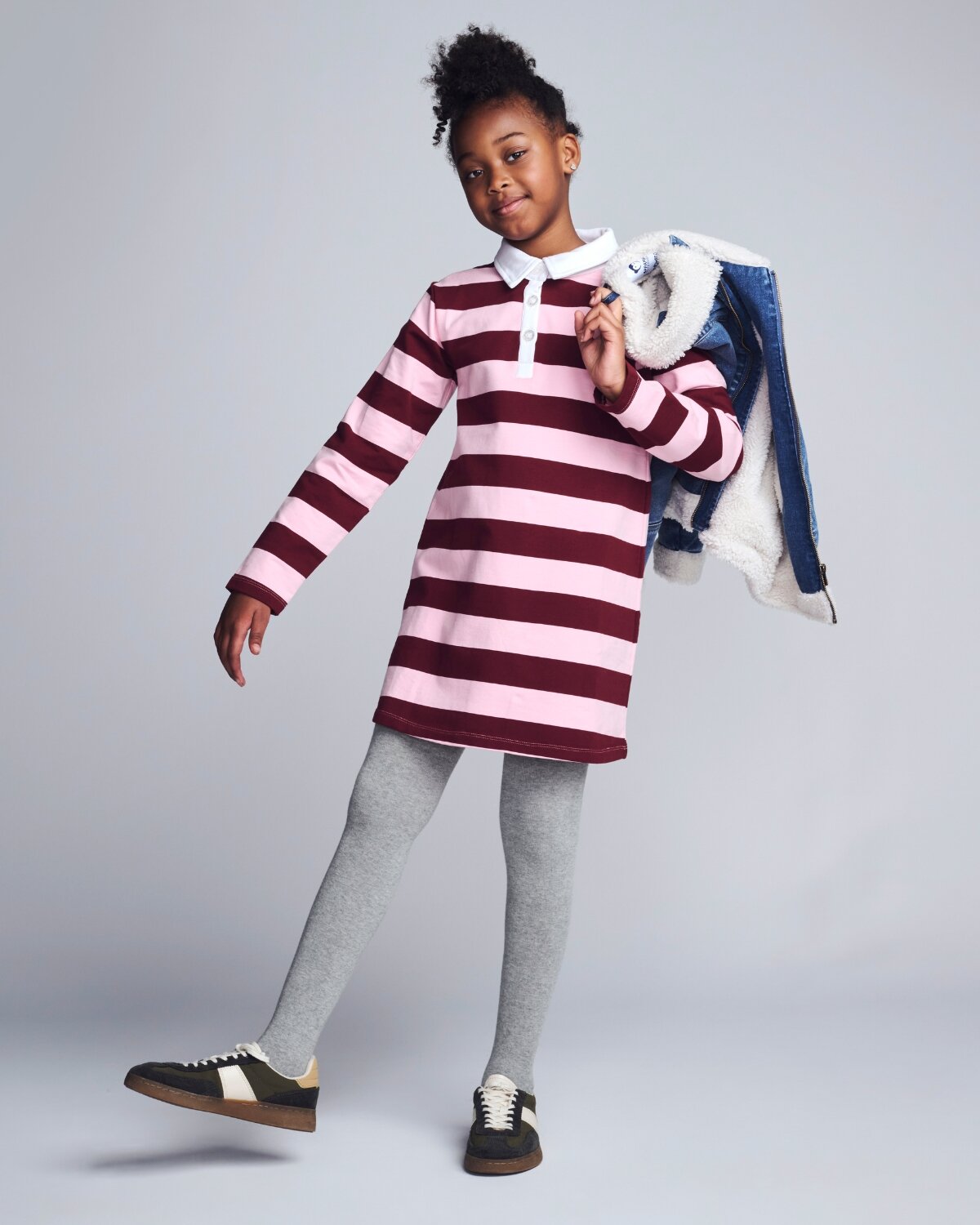 Child wearing a striped dress holding a jacket against a gray background